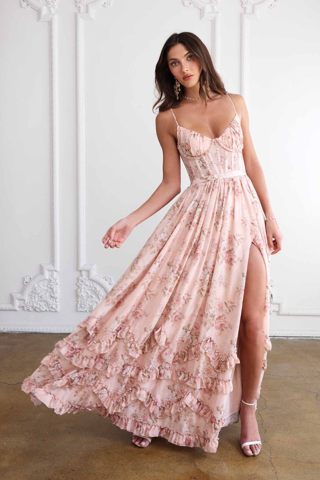 Woman wearing a pink floral dress with a slit in a decorative room.