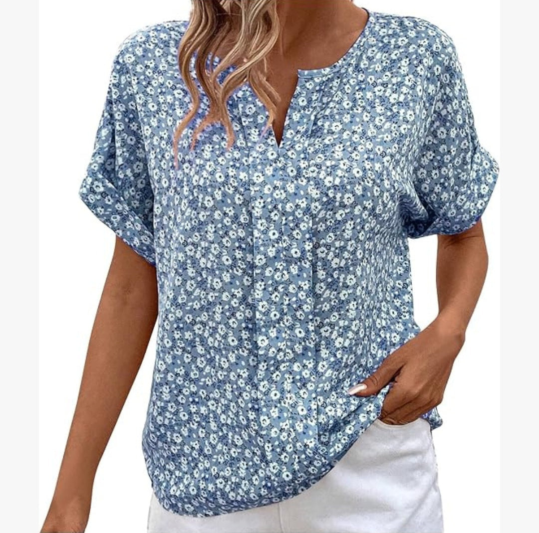 Woman wearing a blue floral blouse with white pants on a plain background
