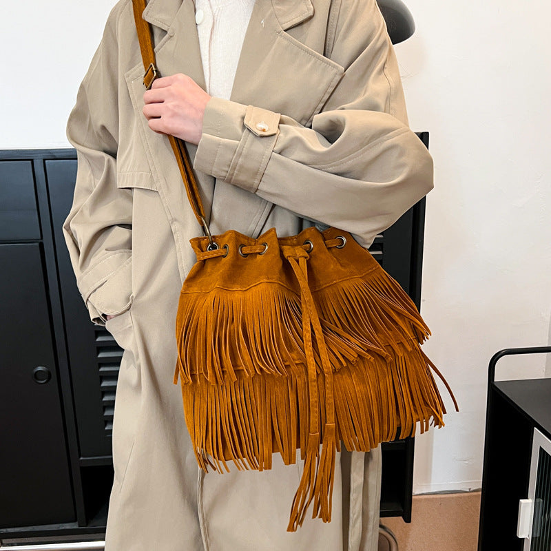 Person holding a brown fringed handbag in an indoor setting