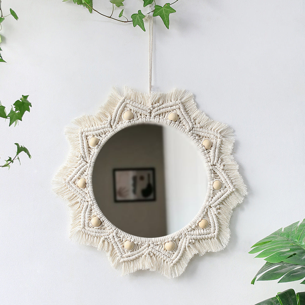 Decorative wall mirror with macrame frame on a white wall with greenery.