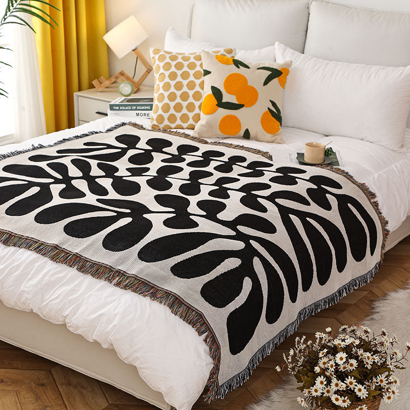 Decorative black and white patterned throw blanket on a bed with pillows and a lamp.