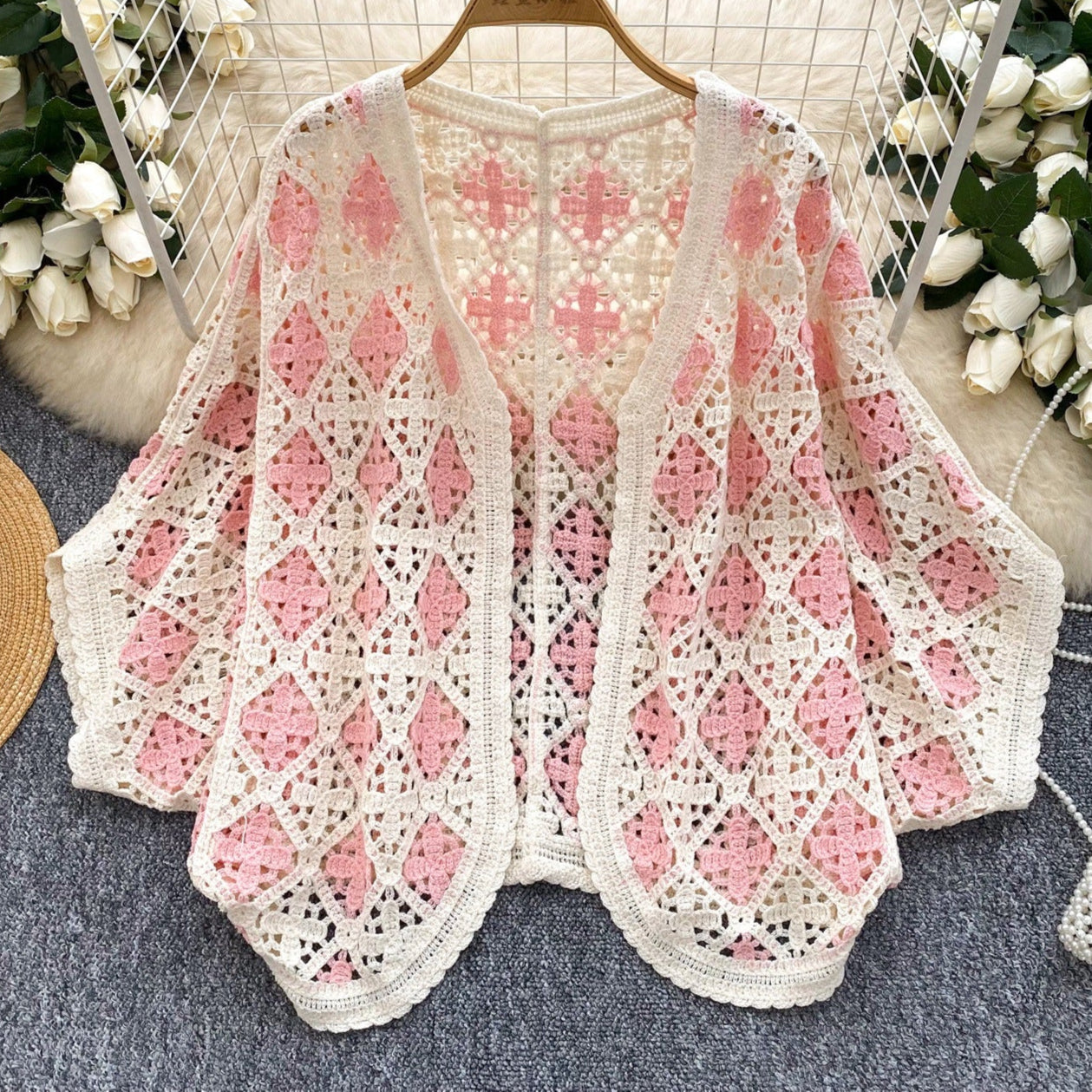 Crocheted pink and white patterned top on a hanger with decorative flowers and a hat in the background.