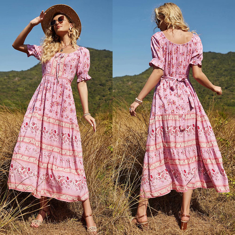 Woman in a pink floral dress standing in a grassy field with mountains in the background
