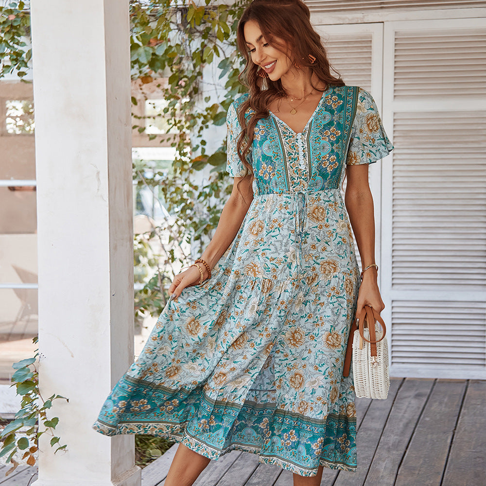 Woman wearing a floral dress standing on a wooden deck with plants in the background