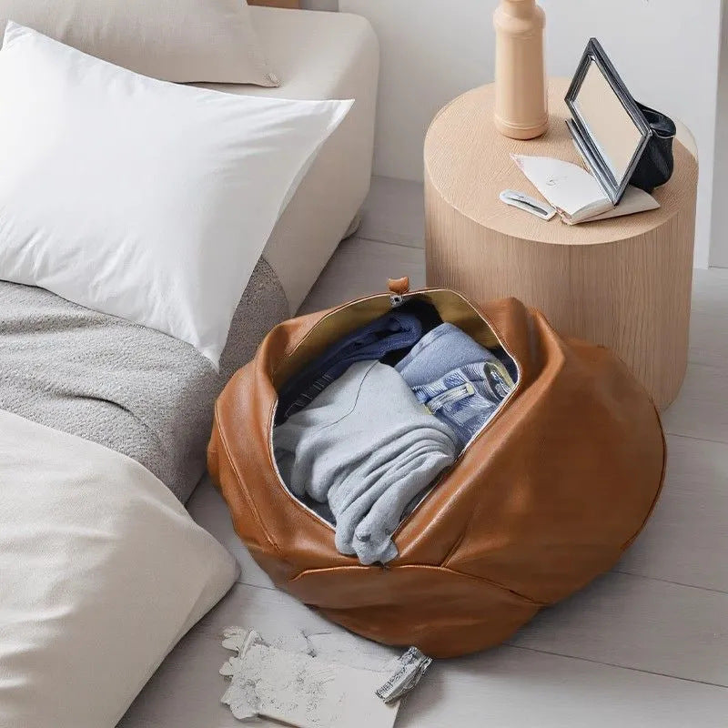 Brown leather storage bag filled with clothes on a light wooden side table next to a sofa.