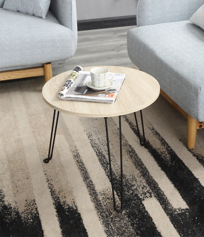 Round wooden coffee table with a magazine and cup on a striped rug in a living room.