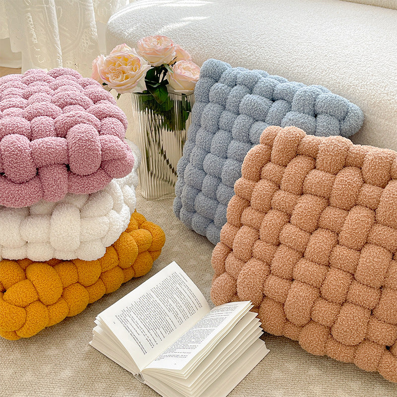 Stack of colorful knitted cushions on a sofa with an open book and flowers.