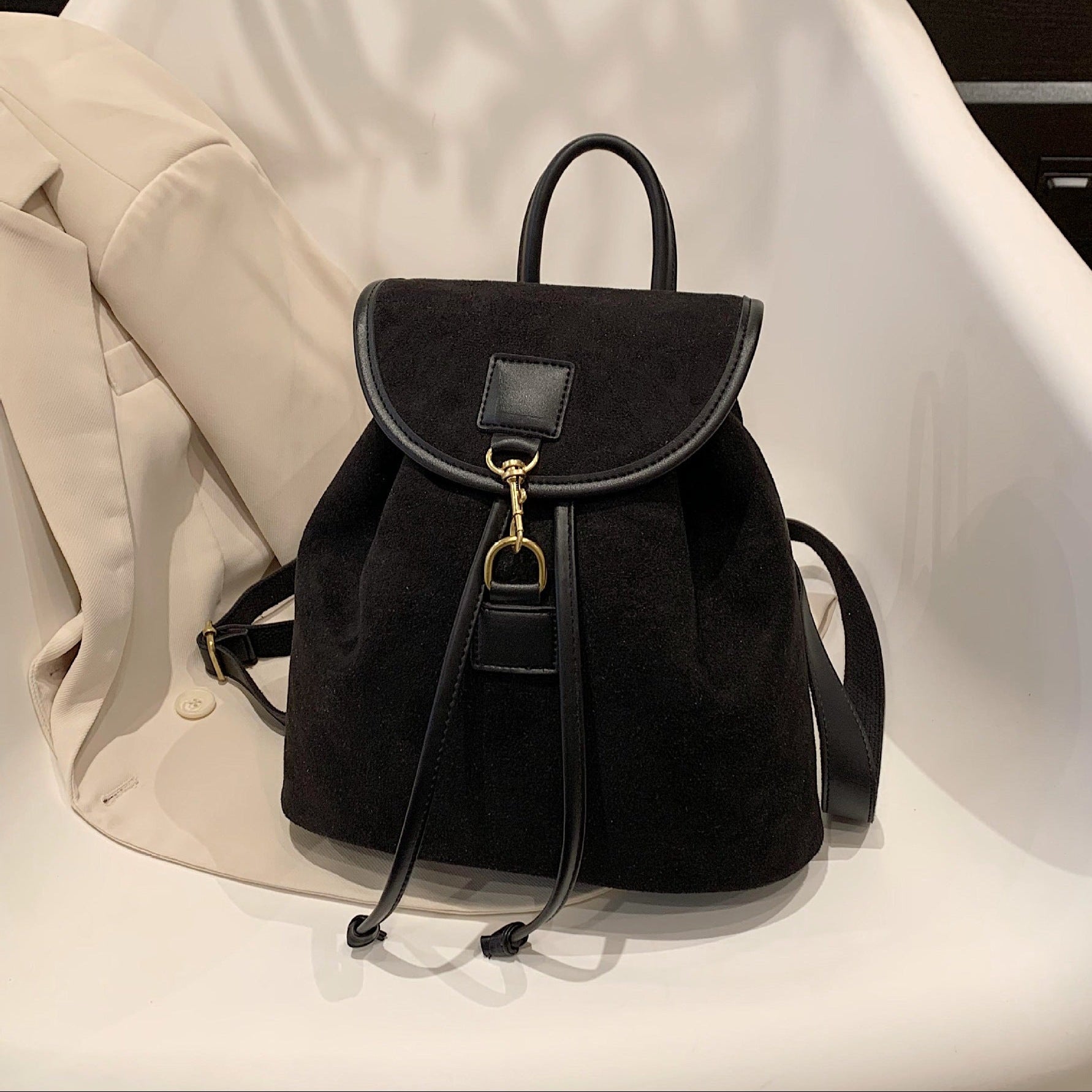 Black backpack on a white surface with a beige coat partially visible