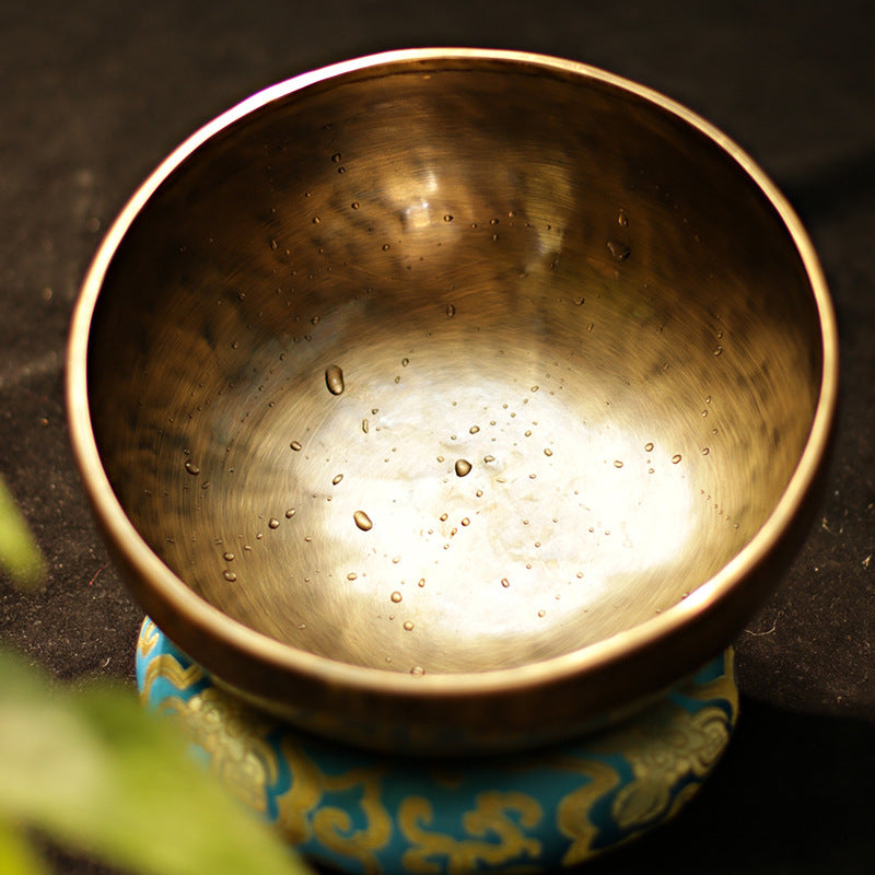 Bronze singing bowl with water droplets on a dark surface