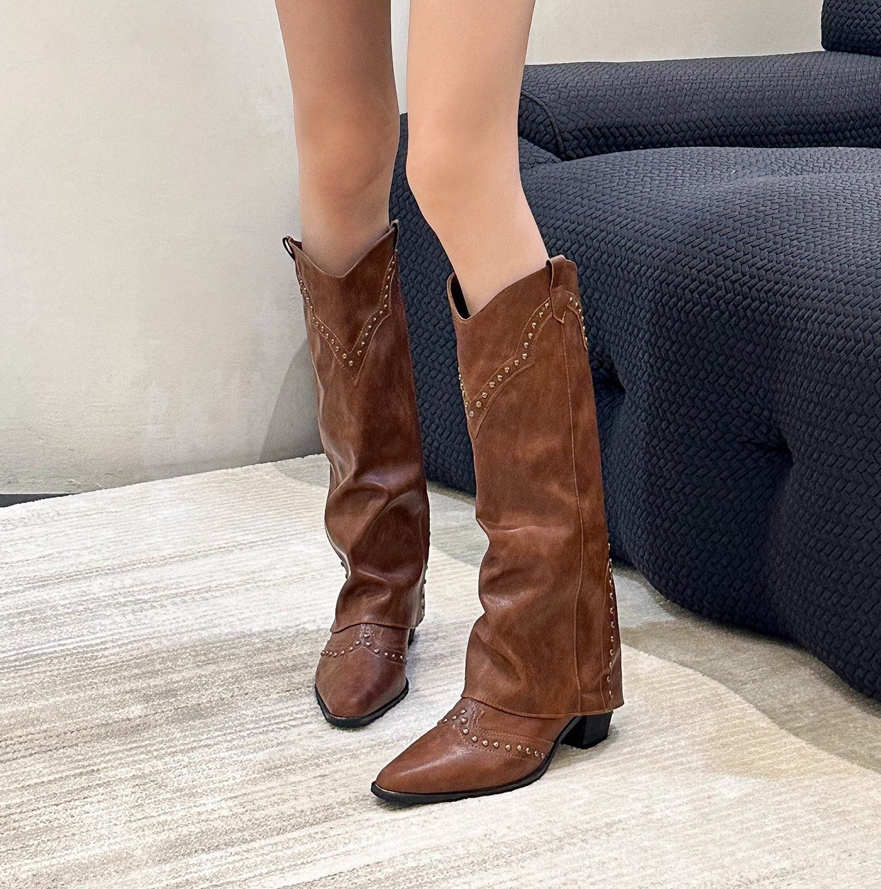 Person wearing brown knee-high boots in a room with a sofa and books.