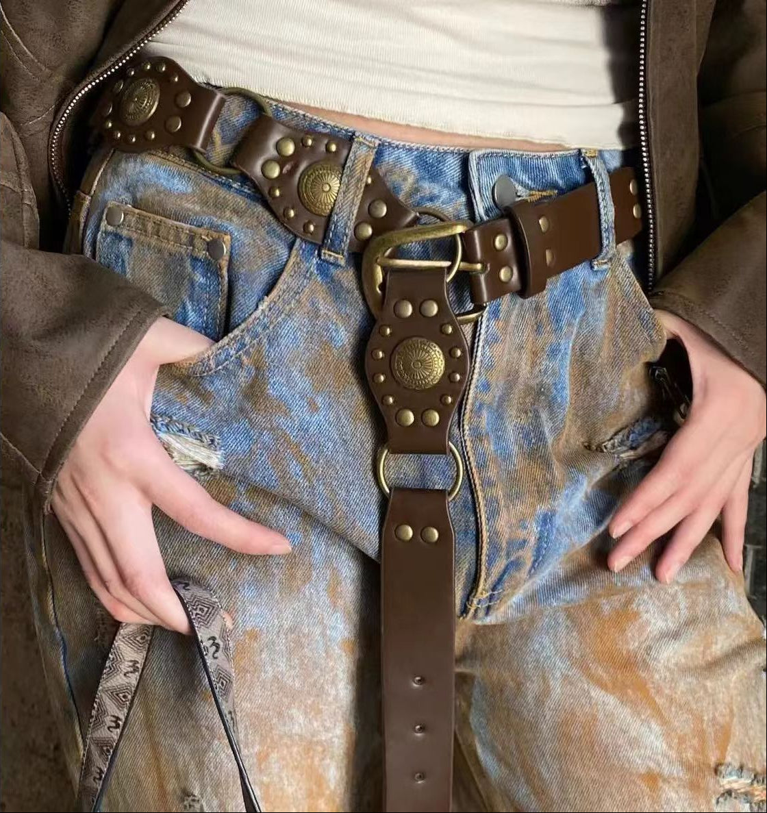 Close-up of a person wearing blue jeans with a brown belt featuring large buckles.