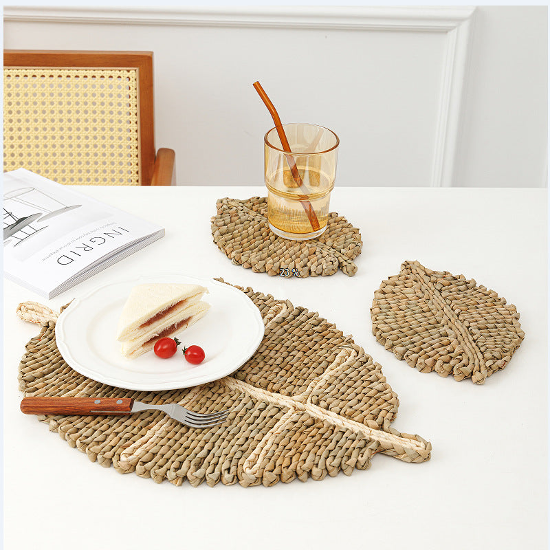 Woven placemats and coasters on a table with a glass of water and a sandwich.