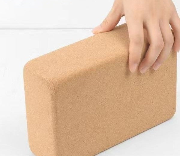 Brown yoga block with a hand holding it on a white background