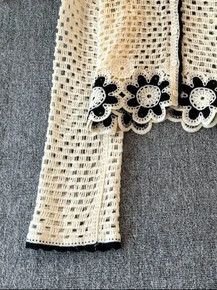 Beige crochet cardigan with black floral details on a hanger.