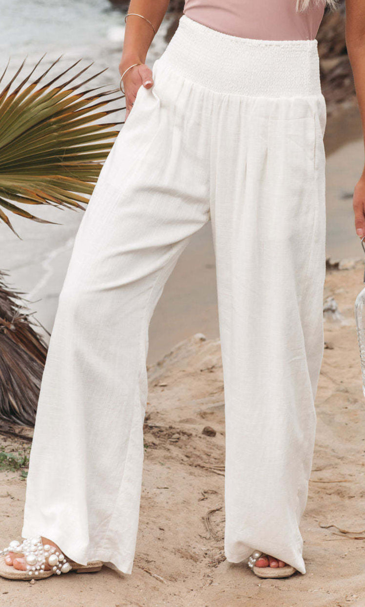 Person wearing white pants holding a water bottle on a beach.