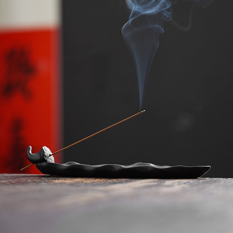 Incense stick with smoke on a black dish against a dark background