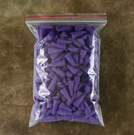 Clear plastic bag filled with purple plastic caps on a brown surface
