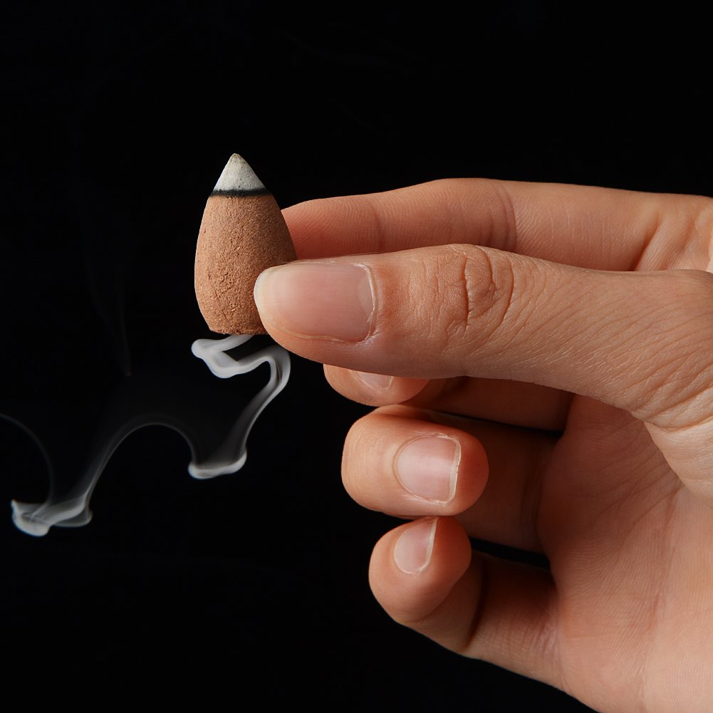 Hand holding an incense cone with smoke against a black background