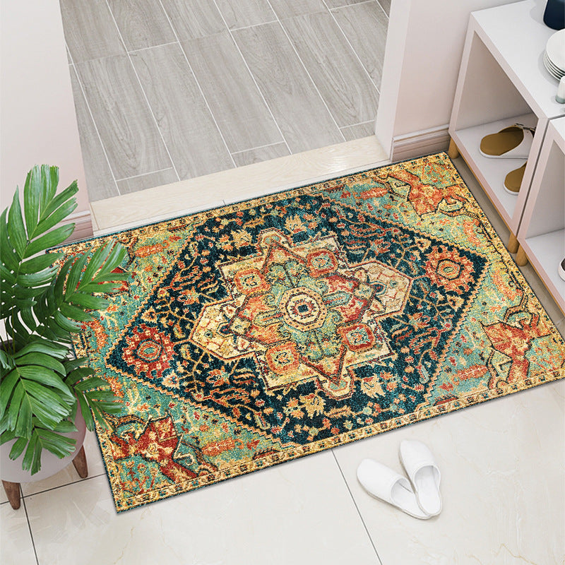 Decorative rug with intricate patterns on a tiled floor, next to a plant and a pair of slippers.
