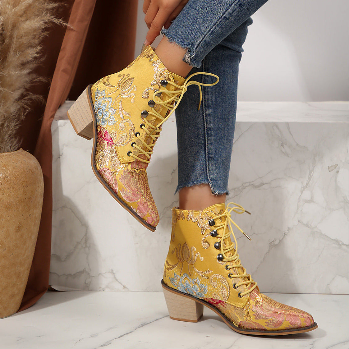 Yellow embroidered boots being worn on a marble floor with a plant in the background