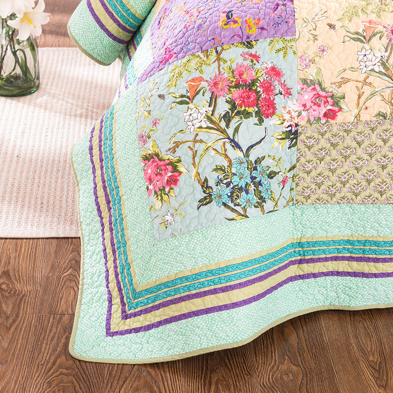 Colorful floral quilt on a wooden floor with a vase of flowers in the background