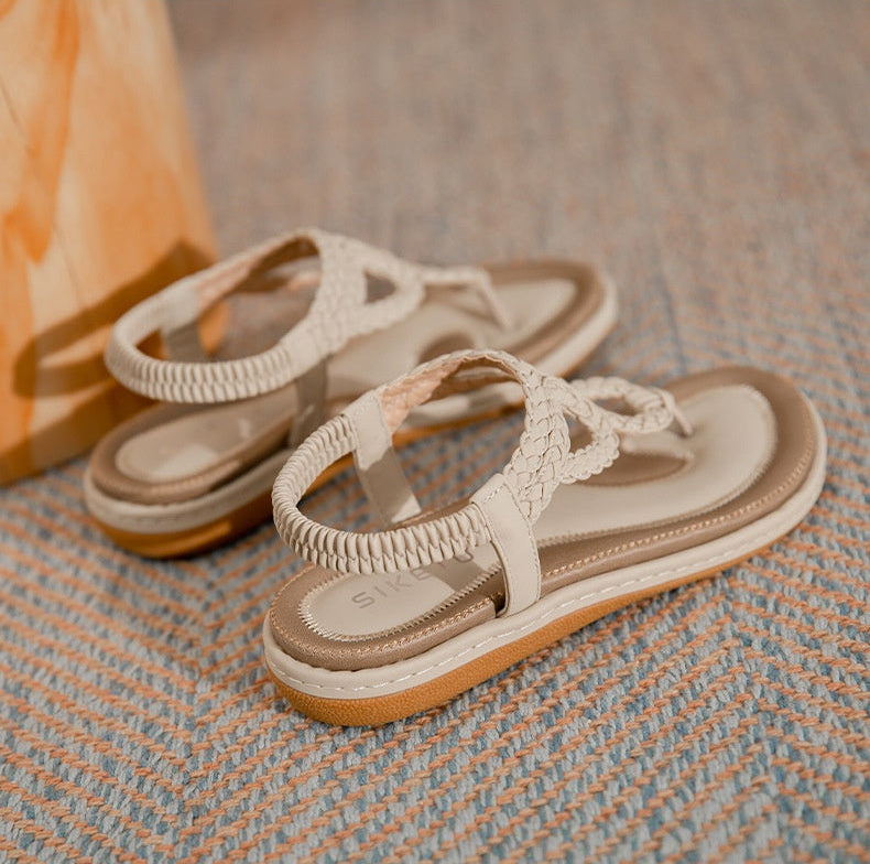 Pair of beige sandals with braided straps on a textured surface