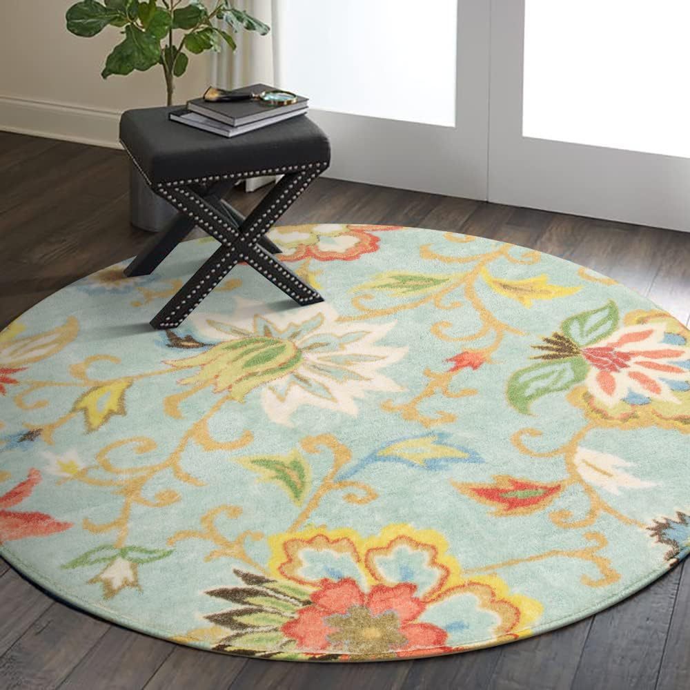 Round floral rug on a wooden floor with a black stool and plant in the background.