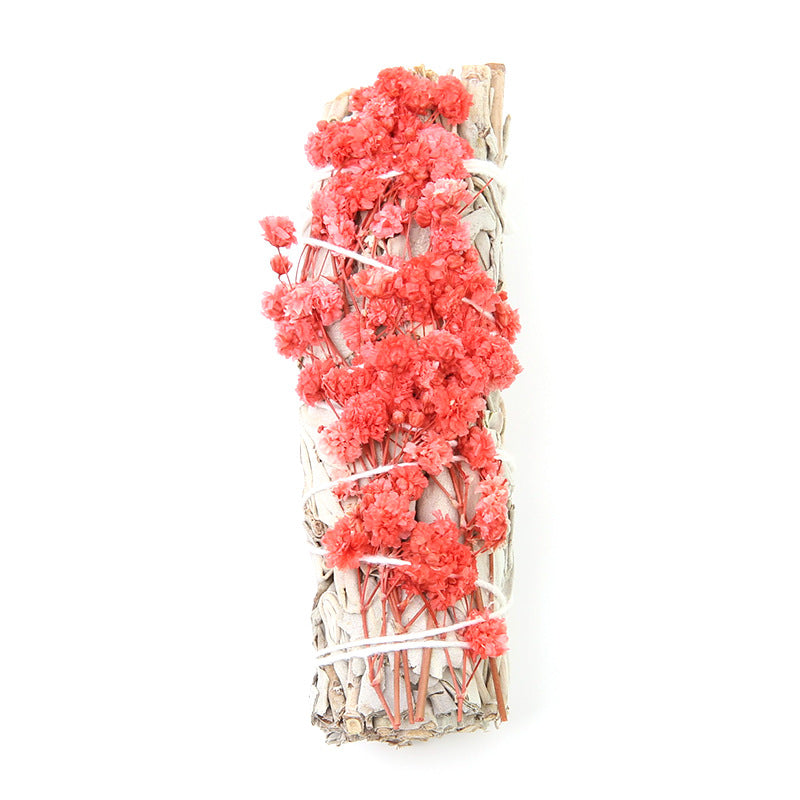 Decorative arrangement of pink flowers and white branches in a clear glass vase on a white background