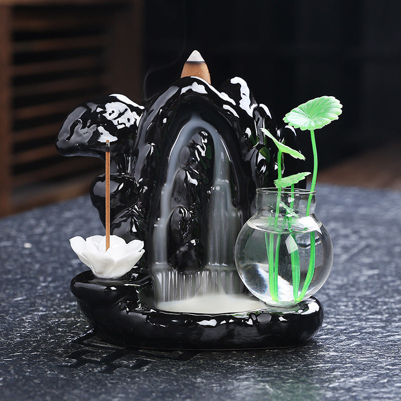 Decorative incense burner with water fountain and plants on a dark surface