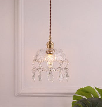 Decorative pendant light with clear glass shade and brass fixture on a neutral background.