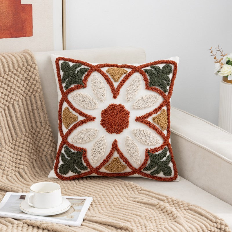 Decorative pillow with a floral pattern on a couch with a blanket and cup of coffee.