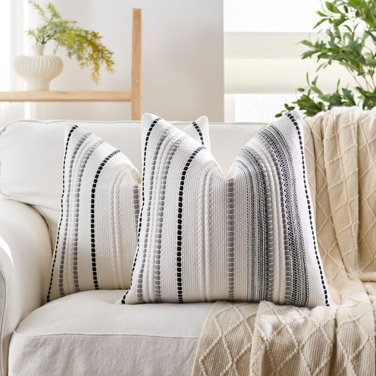 Decorative pillows with black and white stripes on a white sofa in a bright living room.