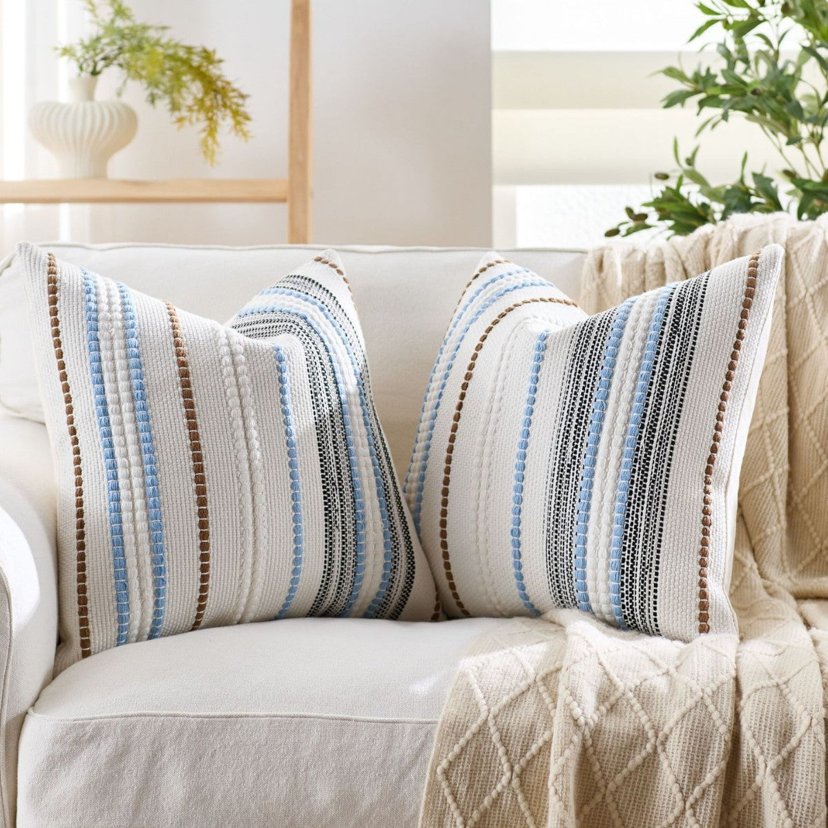 Decorative pillows with striped pattern on a beige sofa in a bright room.