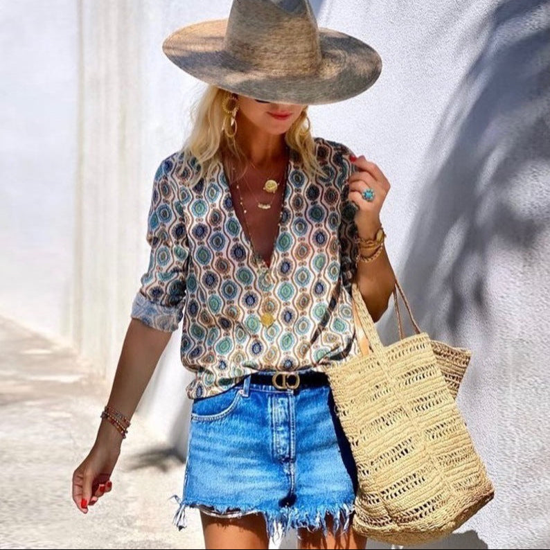 Woman wearing a patterned blouse, denim shorts, and a straw hat, holding a straw bag.