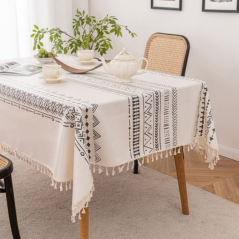 Dining table with a patterned tablecloth, chair, and plants in a room.