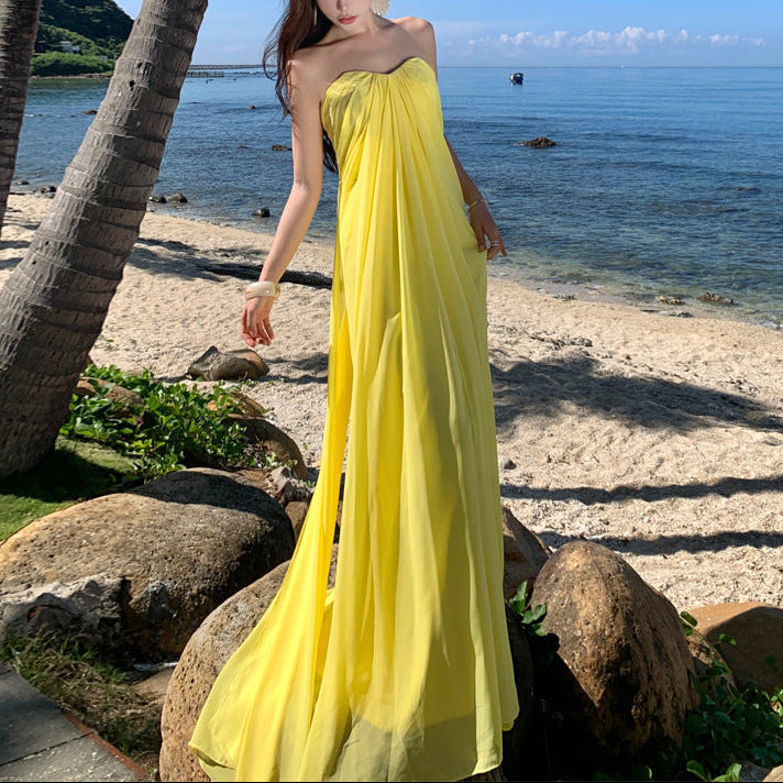 Woman in a yellow dress standing on a beach with palm trees and ocean in the background