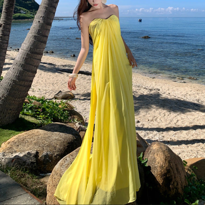 Woman in a yellow dress standing on a beach with palm trees and ocean in the background