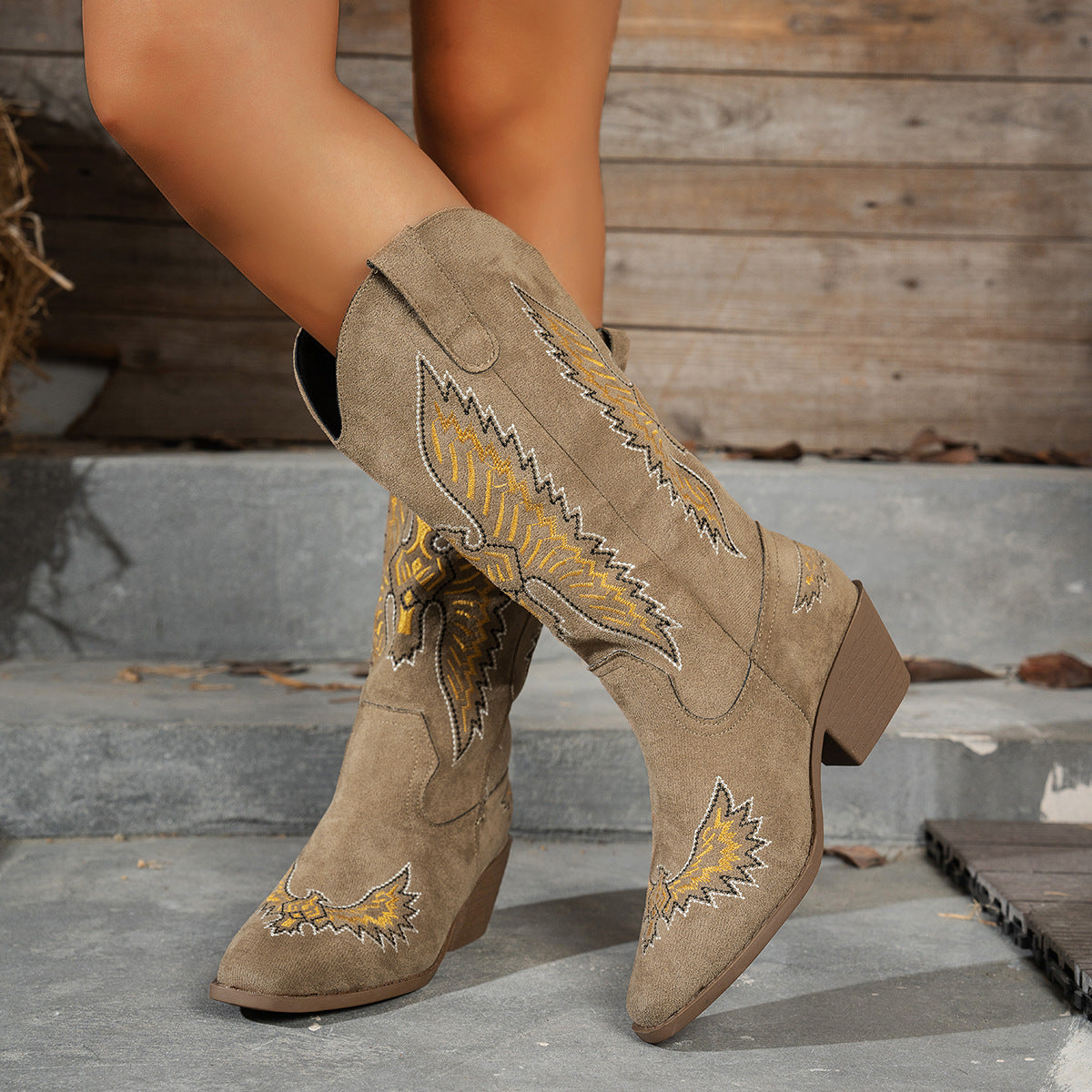 Brown suede cowboy boots with gold embroidery on a wooden background
