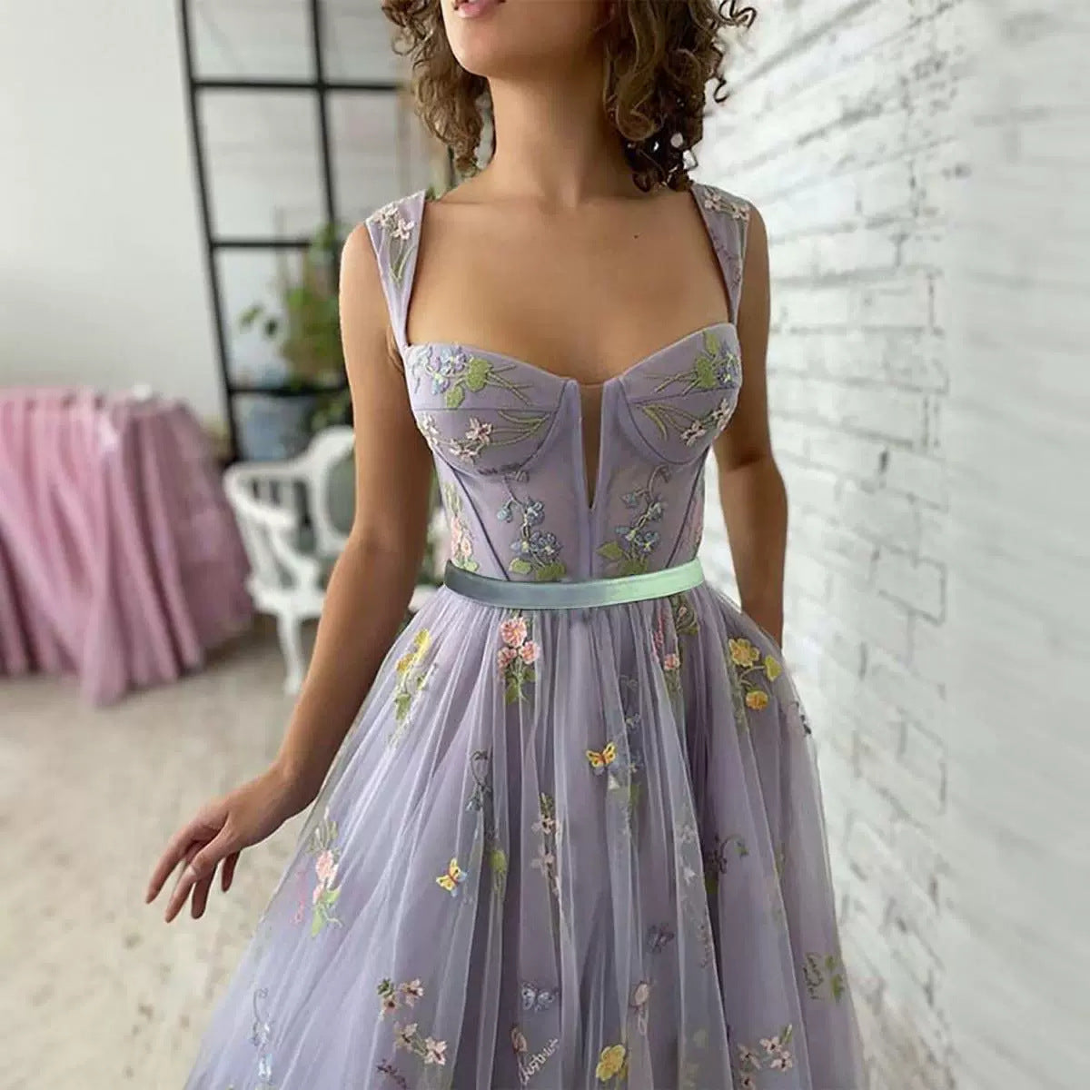 Woman wearing a lavender dress with floral embroidery in an indoor setting.