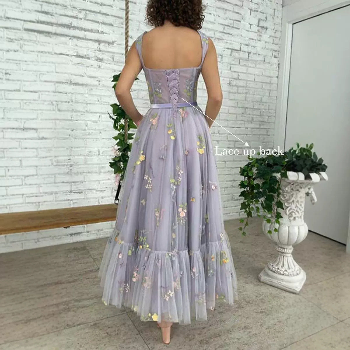 Woman wearing a purple floral dress with a lace-up back in an indoor setting.