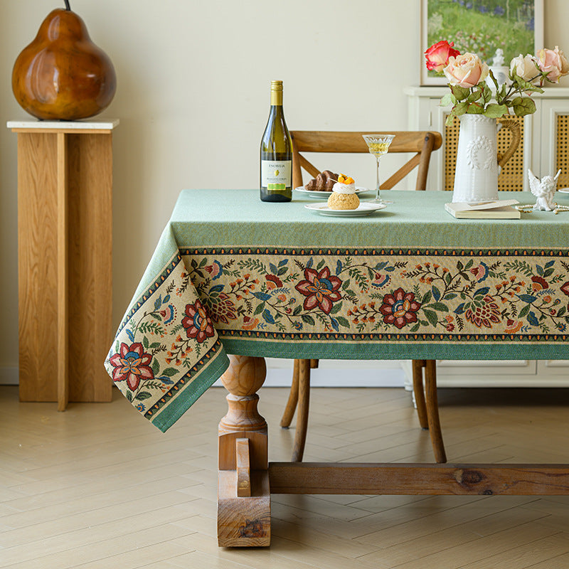 Decorative tablecloth with floral pattern on a wooden table in a room.