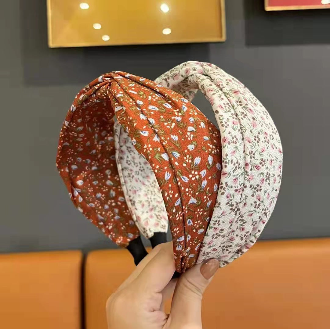 Two floral-patterned headbands held by a hand against a neutral background