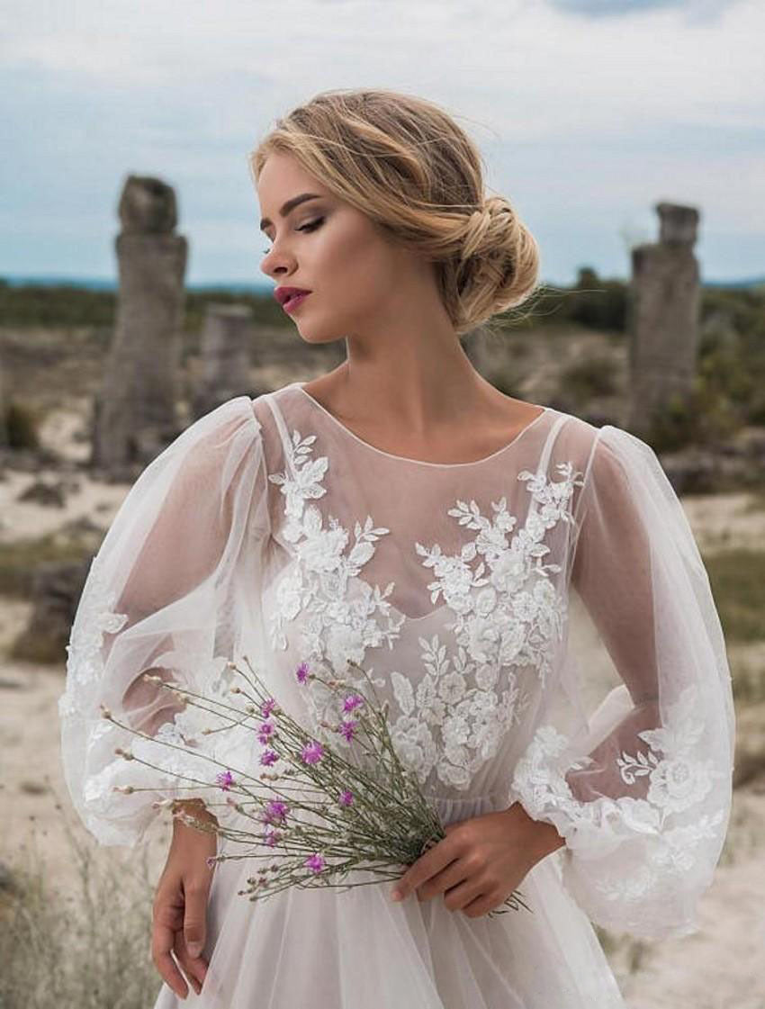 Woman in a white lace dress holding flowers in a desert-like setting