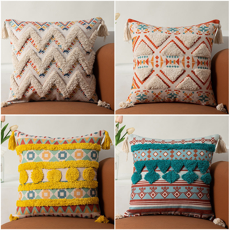 Four decorative pillows with geometric patterns and tassels on a sofa.