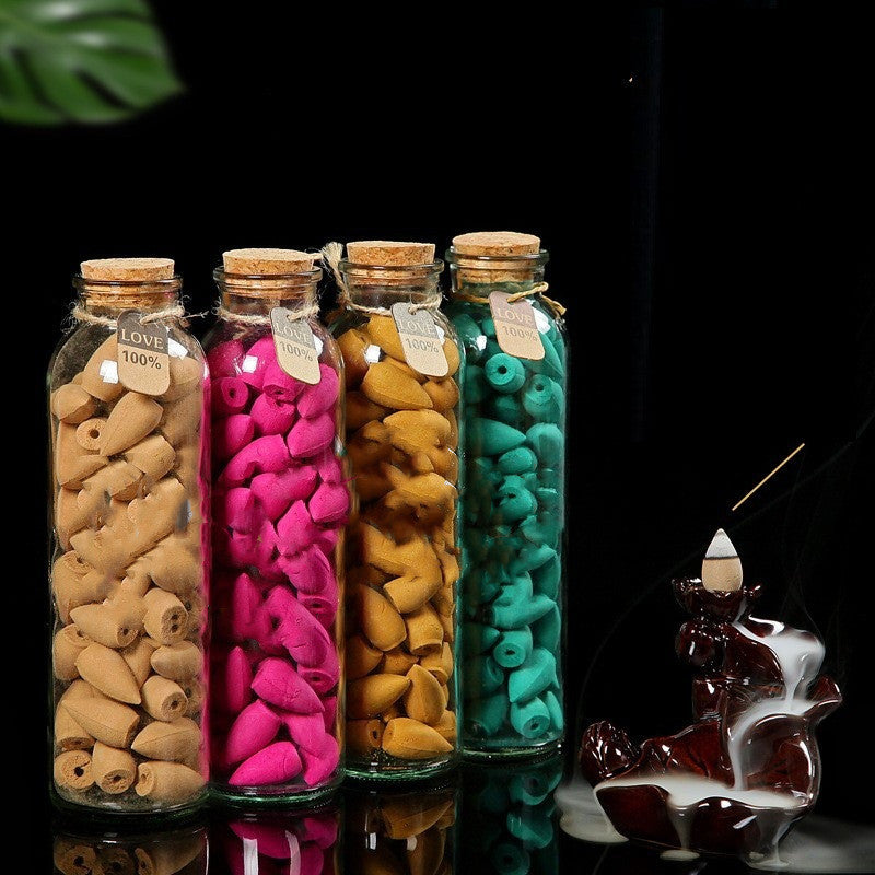 Four glass bottles with cork lids containing colorful incense sticks, with a dark background.