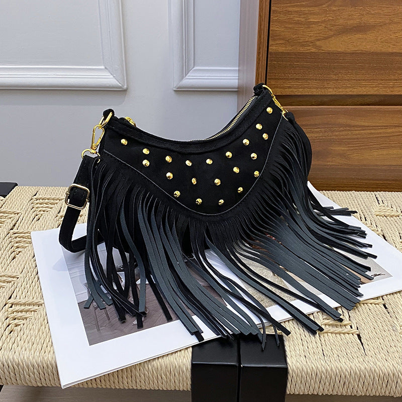 Black fringe handbag with gold studs on a textured surface