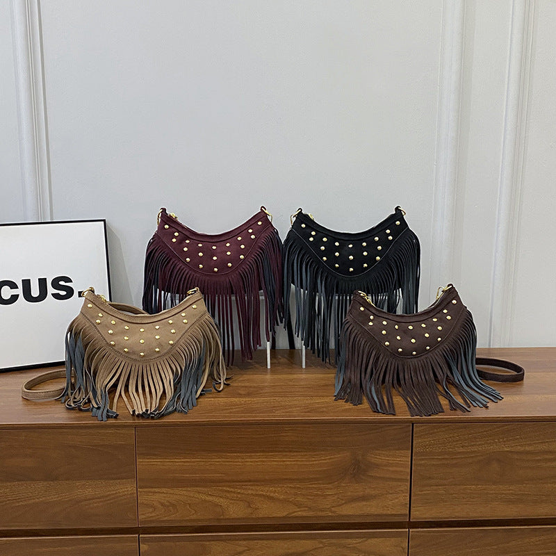 Four fringe bags in different colors on a wooden surface with a white wall background.