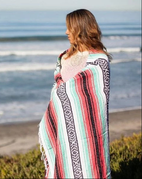 Woman wrapped in a colorful striped blanket standing on a beach.