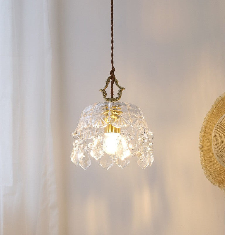 Glass pendant light with a clear bulb inside, hanging against a neutral background.