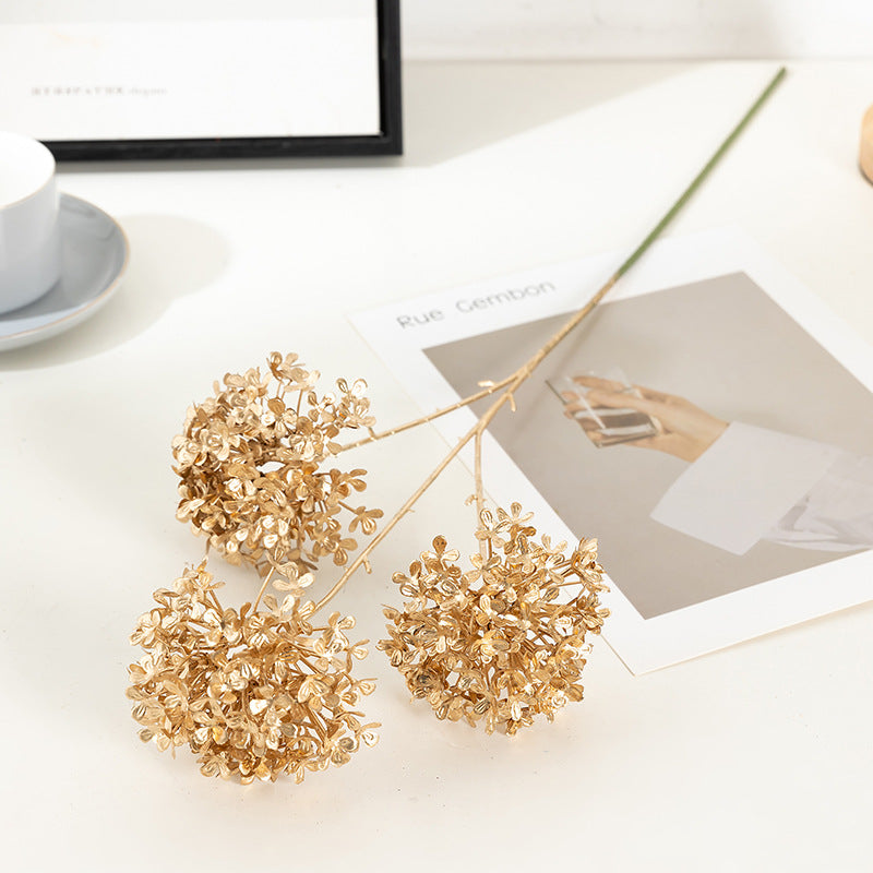 Decorative gold branches on a white surface with a blurred photo and cup in the background